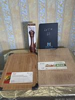 Photo showing two cutting boards, bamboo and wood, and a boxed dark colored pepper mill