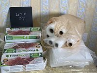 Multiple boxed FoodSaver heat-seal vacuum sealer rolls (2 rolls per box) displayed alongside unboxed rolls and vacuum bags.