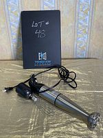Hand blender body with power cord and detachable blending wand lying next to original box