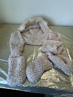Light brown plush sherpa hooded scarf spread out on surface, showing faux fur trim on hood and paw-shaped mittens at ends.