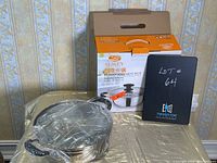 Photo showing stainless steel pot outside box, wrapped in plastic, with box and lot # board behind it.