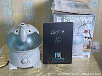 Photo showing the humidifier in shape of an elephant next to its original box and lot marker.
