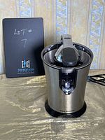 Cool Kitchen juicer showing front view with stainless steel body, black lever handle on top, and power switch area.