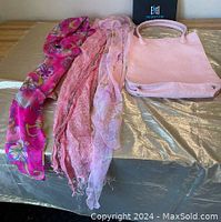Photo showing the pink handbag alongside three scarves with different patterns and textures on a table.