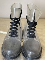 Front view of both transparent lace-up rain boots, showing black laces, toe caps and soles.