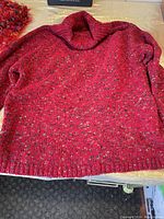 Red speckled turtle neck sweater laid flat on surface