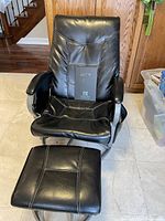 Front view of black faux leather rocking chair with ottoman on a tiled floor.