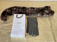 Faux fur scarf laid out with charcoal grey leather gloves and branded paper bag