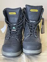 Front view of the black Stanley work boots with visible Stanley logo on the tongues and black laces.