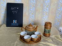 Photo of tea set including teapot, cups, tray, and loose tea holder arranged on fabric surface with black board displaying lot number 44 in background.