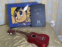 Photo showing the Hilo ukulele on a table with the Mighty Atom towel set in the background in its box.