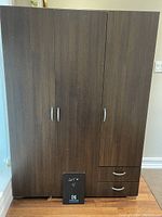 Front view of a three-door wooden wardrobe with two drawers on one side, showing overall condition and design.