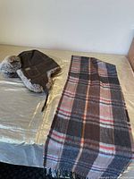Windriver trapper winter hat with faux fur lining and ear flaps next to a plaid scarf on a table.
