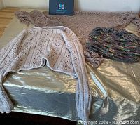 Photo showing all three items: the taupe crocheted shawl spread out behind, the cream crocheted sweater centered in front, and the multicolored woven purse to the right of the sweater.