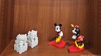 Full view showing the pair of white stone foo dogs on the left and the colorful Minnie and Mickey Mouse kissing bobble-head figurines on red bases on the right.