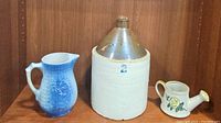 Photo showing the lot of three items: antique 2 gallon jug with salt glaze, blue stoneware pitcher, and yellow rose ceramic pitcher.