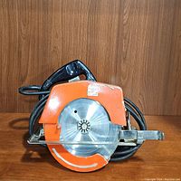 Front view of vintage Power House circular saw showing orange blade guard, stainless steel blade and black handle