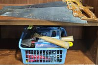 Basket containing hammers, nails, and small hand tools, including pliers and screwdrivers, alongside the two large saws above.