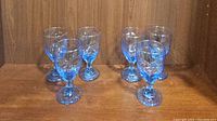 Set of six blue Libbey Chivalry patterned water goblets arranged in two rows on a wooden surface with a wood grain background.