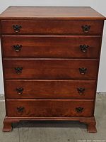 Front view of mahogany chest showing five drawers with metal handles and bracket feet.