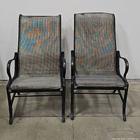 Front view of two woven metal patio chairs placed side by side, showing woven mesh seats and backs with black metal frames and armrests.