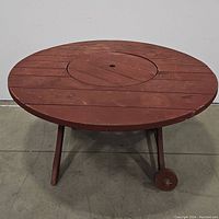 Front view of the reddish-brown round wooden table with visible wheels on one side and central removable section.