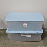 Two Sterilite brand plastic storage containers stacked, showing frosted translucent sides and light blue lids.