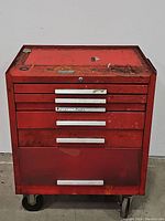 Front view of closed red rolling tool chest showing wear, rust, and silver metal drawer handles.