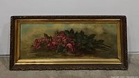 Full view of the horizontal painting of pink and red long stem roses with green leaves in an ornate gold frame.