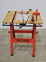 Front view of the vintage Hirsh saw table showing wooden top, cutout center, red metal frame, adjustment knobs and clamp.