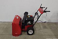 Side view of red snow blower showing auger housing, engine and handle assembly
