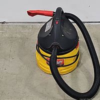 Top side view of Stinger WD2000 wet/dry vacuum showing red handle, red power switch, and coiled black hose attached to front port.