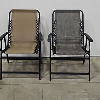 Two suspension folding armchairs side by side, one tan and one dark gray, both with black metal frames and armrests, showing overall condition and design.