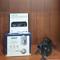 Samsung video camera recorder, Schlage Keypad Security Set box, and digital converter box in packaging on a wooden surface