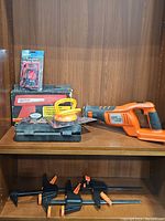 Shelf display showing multiple tools including the Black & Decker reciprocating saw, clamps, dent remover, multimeter in packaging, and a case.