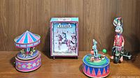 Wide shot showing all four items including the Otagiri carousel music box, Texas cowboy bank, duck wind-up figurine, and circus clown figurine.