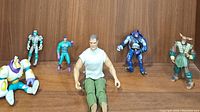 Set of six action figures posed on a wooden shelf, showing variety in character style and color.