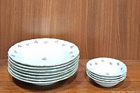 Stack of 6 larger pasta or soup bowls next to a stack of 4 smaller dessert bowls, both with white porcelain and red rose bud pattern along scalloped edges