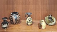 Group photo of five ceramic vases showing various shapes and glaze styles including Corinthian painted vase, stoneware bud vase, and black & gold Greek vase.
