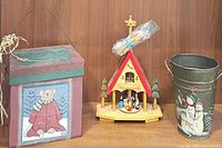 Photo showing all three items: wood alpine carousel, teddy bear lidded box, and metal snowman pail on wooden surface