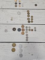 Overview of 40 used coins arranged by country and size on a white wooden surface. Coins vary in metal tonality and wear.
