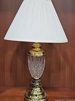 Full view of one crystal urn lamp with white pleated linen shade, showing crystal base and brass fittings.
