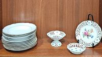 Wide view of eight dinner plates stacked, two pierced decorative bowls, and a Dresden flowers plate on display stand