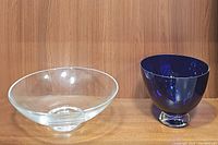 Photo showing the clear glass bowl and blue urn style bowl side by side on wood surface and background.