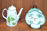 Godinger Jardin porcelain coffee pot with green leaf and insect designs next to green ceramic eagle plate displayed on wooden shelf