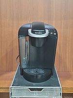 Front view of the black Keurig B40 single cup coffee maker with transparent water reservoir and control buttons on top right.