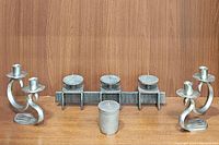 Full view of all five metal candle holders together against a wood background: 3-pillar holder, pair of candlestick holders, votive holder
