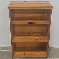 Front view of pine bookcase with three shelves and visible knots on shelf surfaces and back panel.