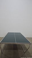 Front view of the folded metal ping pong table showing the dark playing surface and white center lines.