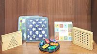Photo of 7 assorted mind puzzle games: wooden triangular peg solitaire, wooden peg board with colored pegs, colorful circular puzzle pieces, and 'Siblet' card set along with plastic tile puzzles.
